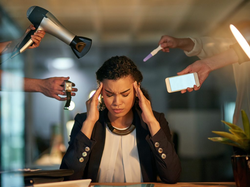 A woman sits at a desk holding her head in frustration, illustrating stress as multiple hands offer her a hairdryer, wristwatch, smartphone, and a pregnancy test.