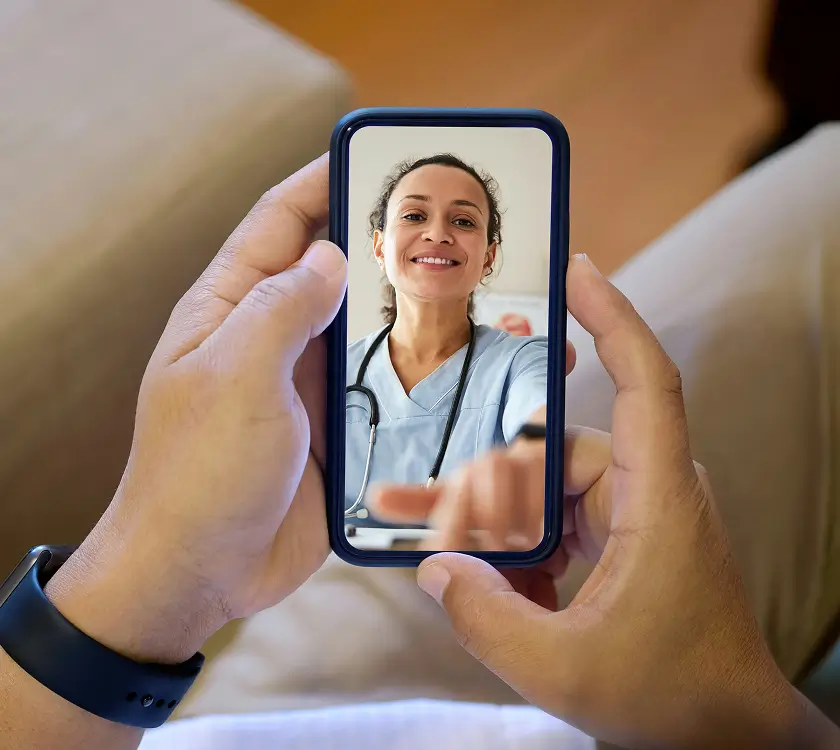 Individual holding a smartphone displaying a video call with a smiling healthcare professional wearing scrubs and a stethoscope.