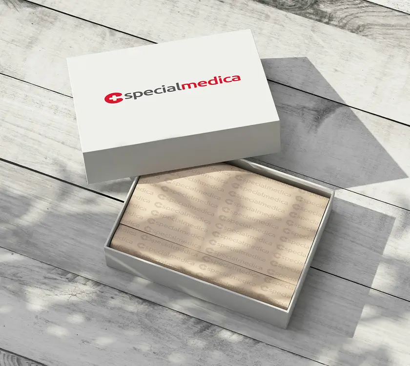 White box labeled "specialmedica" with a partially open lid, showing brown branded wrapping paper inside, placed on a wooden surface with light shadows.